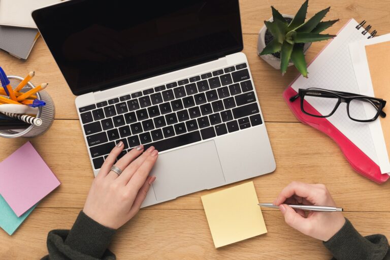 Woman typing on laptop computer and writing notes